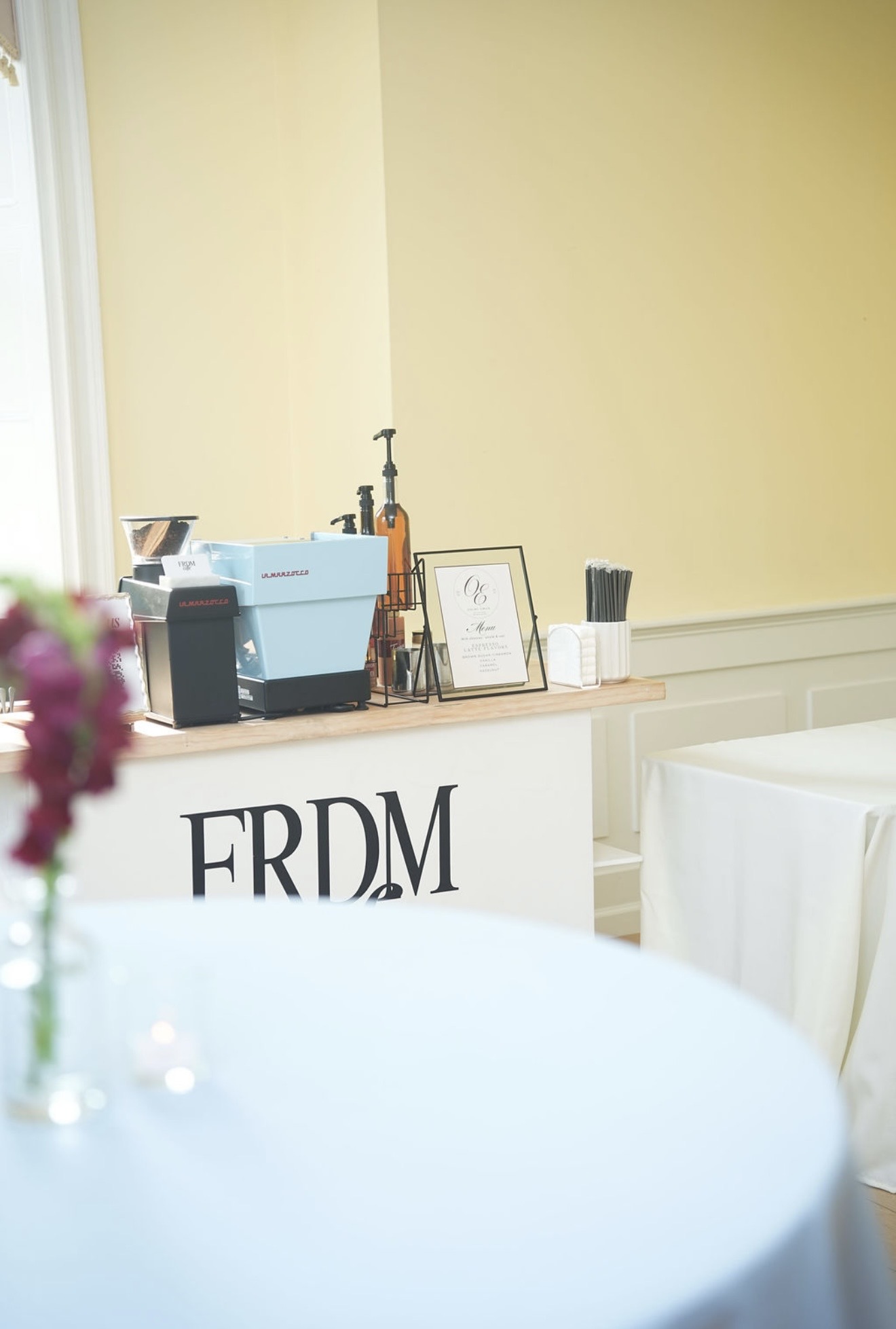A coffee cart with an espresso machine, a framed monogrammed menu and a printed drinks list.