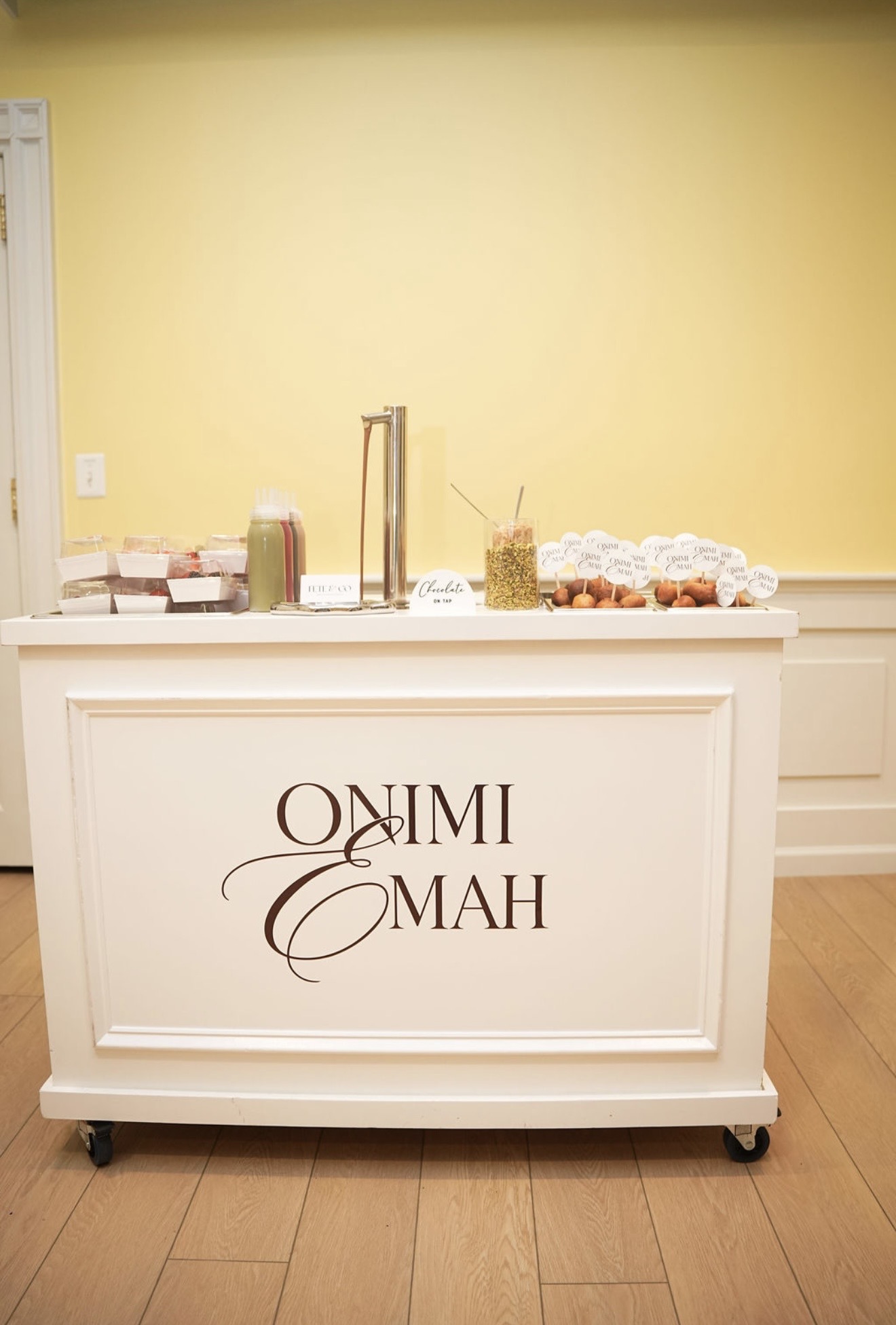 A white cart carrying the Onimi and Emah monogram, set with chocolate on tap and trays of small fried dough.