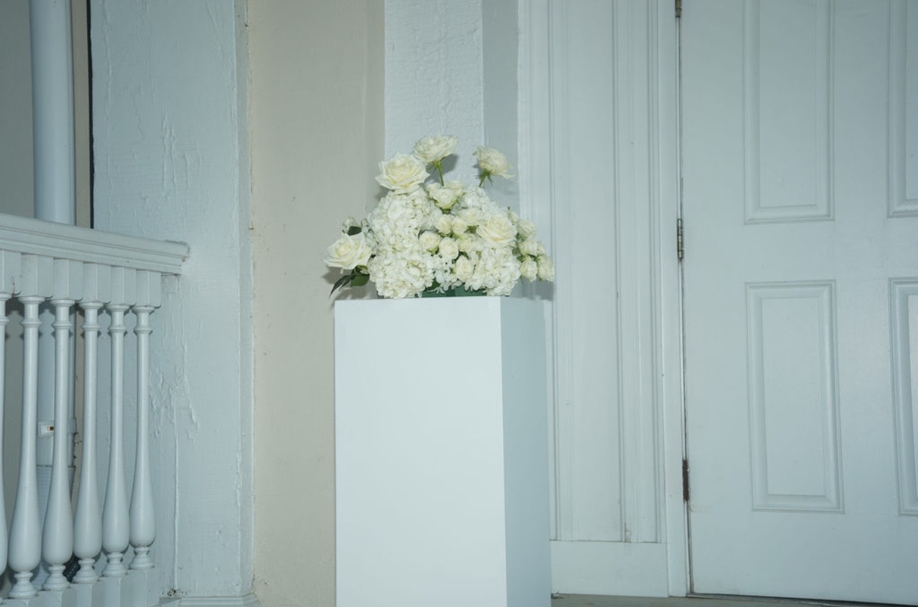 A white pedestal holding an arrangement of white roses and hydrangea against a pale stairwell wall.