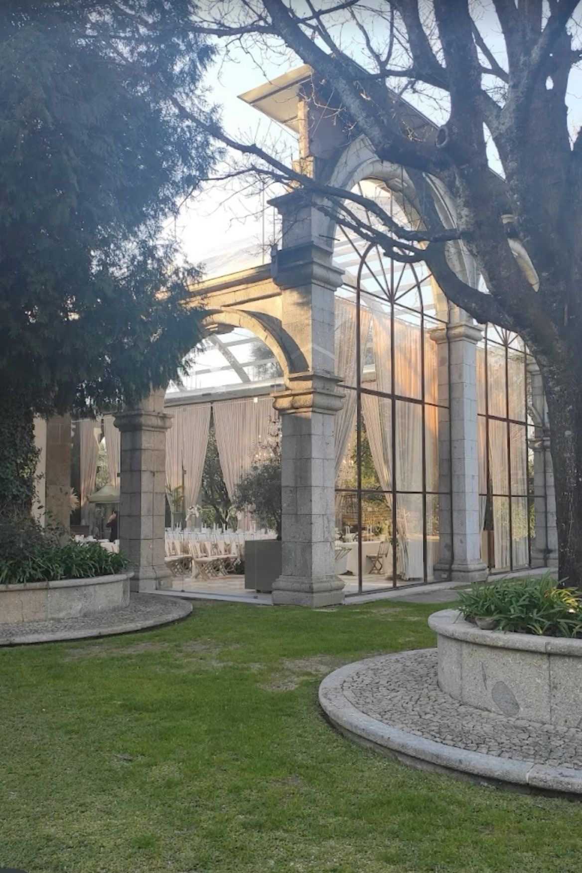 The same stone and glass orangery at dusk, lit from within, seen across the garden.